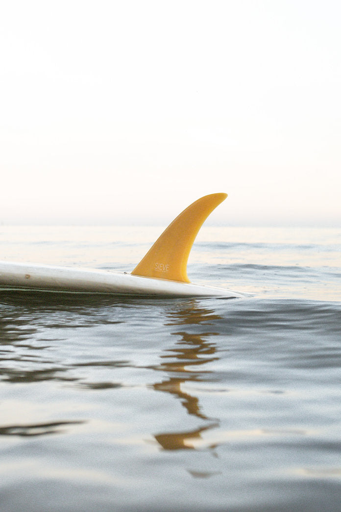 Sustainable Single Fin - 9’6 - color yellow screwed into a longboard floating in the sea